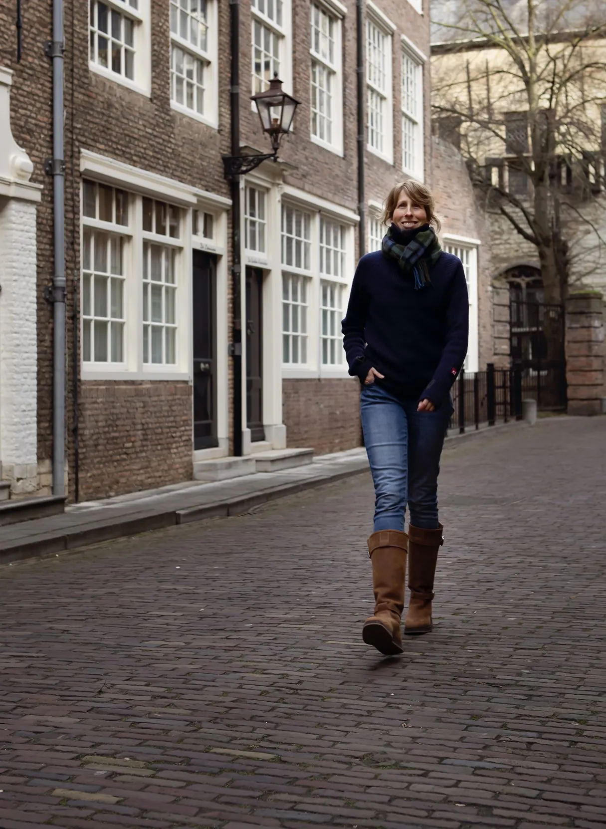 Mies Oude Avenhuis wandelt met een geruite sjaal om door een oude binnenstad