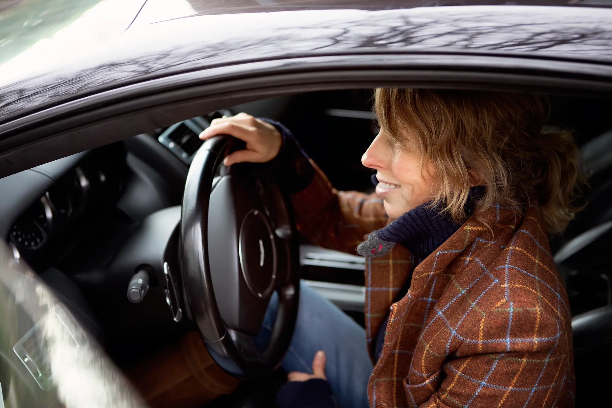 Mies Oude Avenhuis zit lachend achter het stuur van haar auto, onderweg naar een afspraak