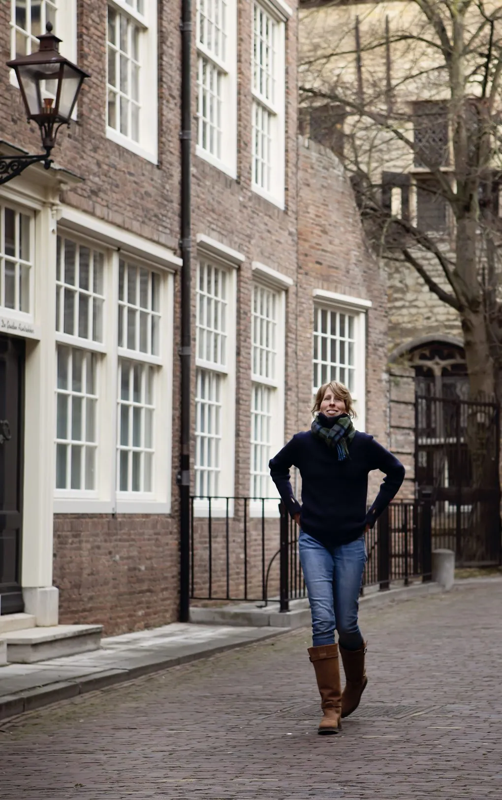 Mies Oude Avenhuis loopt lachend met haar handen in haar zakken door een oude straat